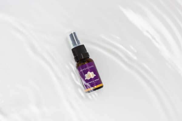 Een klein bruin sprayflesje met het opschrift "MINDSCOPIC - SLEEPWELL SPRAY™ met melatonine (15ml)" met een afbeelding van een vlinder en een paars etiket, geplaatst op een gegolfd wit oppervlak.